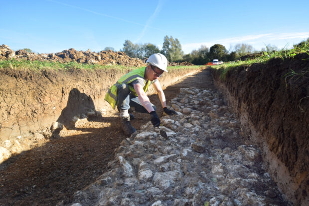 EA archaeologist working in a trench on a stone causeway