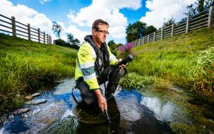 An environment agency officer crouching in a stream conducting water monitoring