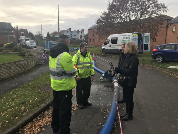 Image of men in high visibility jackets talking to a woman nearby a water pumping.