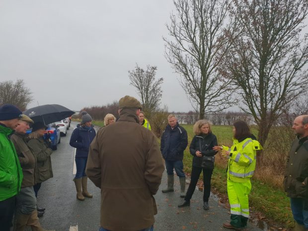 Emma Howard Boyd on a road talking to an Environment Agency officer involve din flood response and wearing hi-vis overalls with a group of people listening nearby