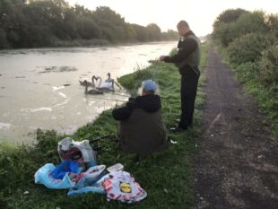 A man is checking the rod licence of an angler sat by a river bank