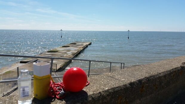 Bottle, container and float equipment for sampling on a sea wall, with beach in background.