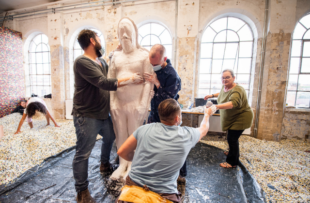 image shows four people handling a life-size human mould, the floor is covered in multi-coloured plastic pellets.