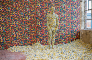 image shows life-size human sculpture made from multi-coloured plastic pellets. 