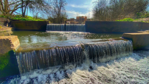 ‘a fast-flowing river running down a weir, in between two grass banks’