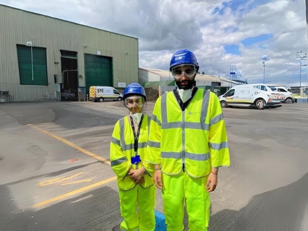 Two Environment Agency officers dressed in yellow high-vis jackets and blue helmets stand outside a regulated site.