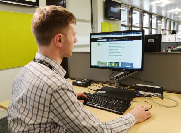 Person at a computer in an office accessing the Environment Agency gov.uk site.