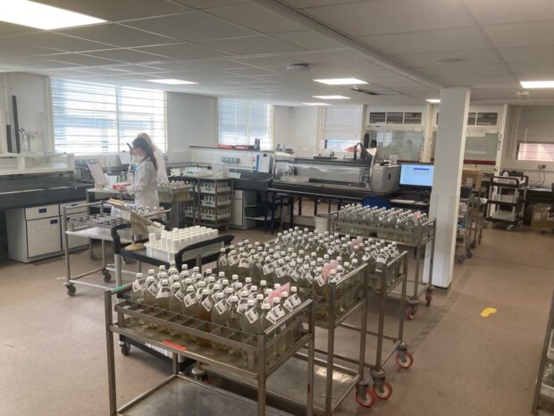 An internal view of the Environment Agency's Starcross labs, with bottles of samples and two scientists working in lab coats in the background.