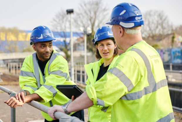 A group of Environment Agency staff wearing blue hard hats and high visibility clothing in conversation