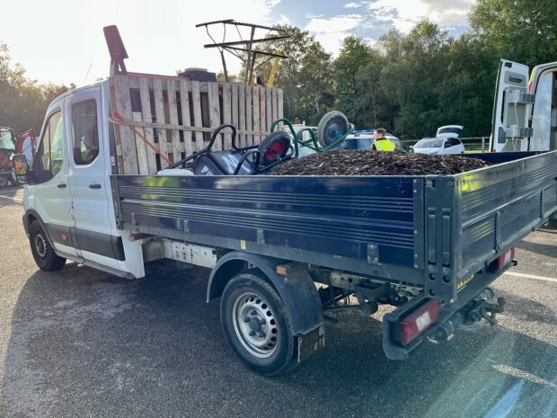 An open-top flatbed vehicle with various types of waste in its cargo area.