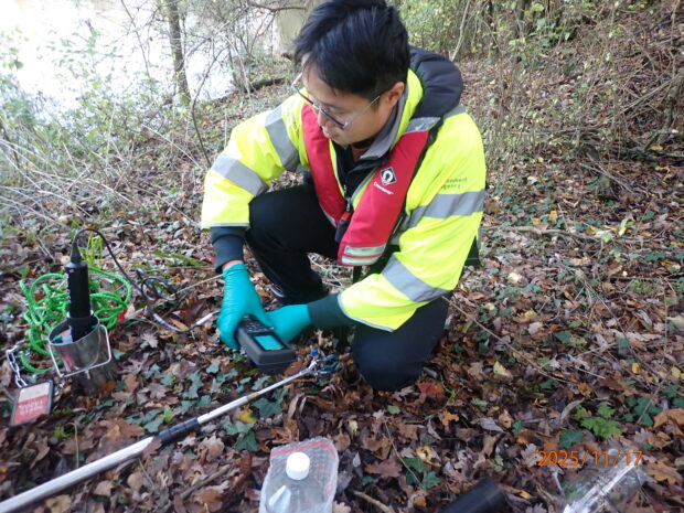 An Environment Agency officer reviews a sample on the edge of a river using monitoring equipment.