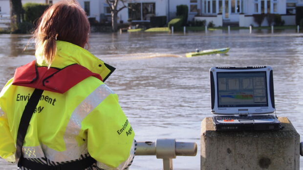 An ARC-Boat, a remote control boat used by the Environment Agency's hydrometry team in a river. An EA operator in the foreground with a laptop displaying results.