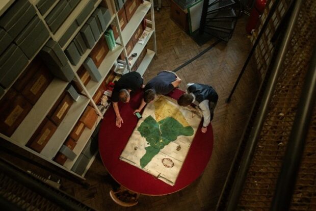 Three people leaning over an ancient map in a room inside Alnwick Castle. 