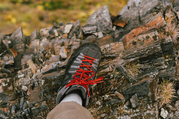 A close-up, aerial photo of a hiker's grey boot with red shoelaces as they stand on a rock.