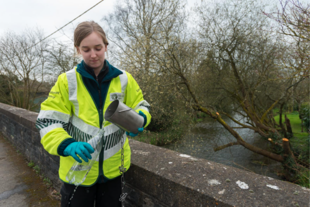 An Environment Agency officer pours a sample from a bucket into a bottle.