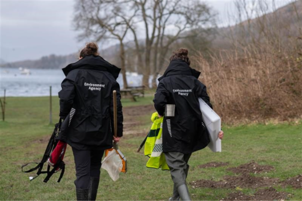 Two Environment Agency staff with equipment in hand walk towards Windermere. 