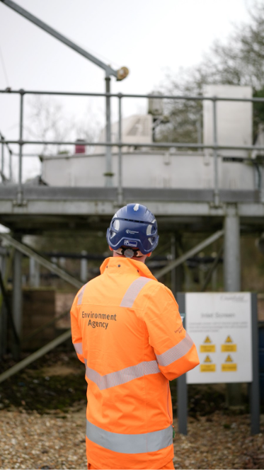 A man in hi vis Environment Agency branded clothing looks around a site.