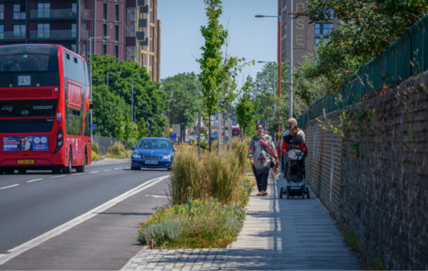 Pedestrians walking along a main road, next to a SuDS feature.