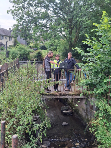 Environment Agency officers standing on a bridge working to identify misconnections at Mill Beck.